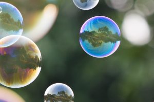 soap bubbles reflecting pink, blue and golden yellow around their circumference, float against a deep green forrest backdrop. In each bubble can be seen a tiny refracted forest